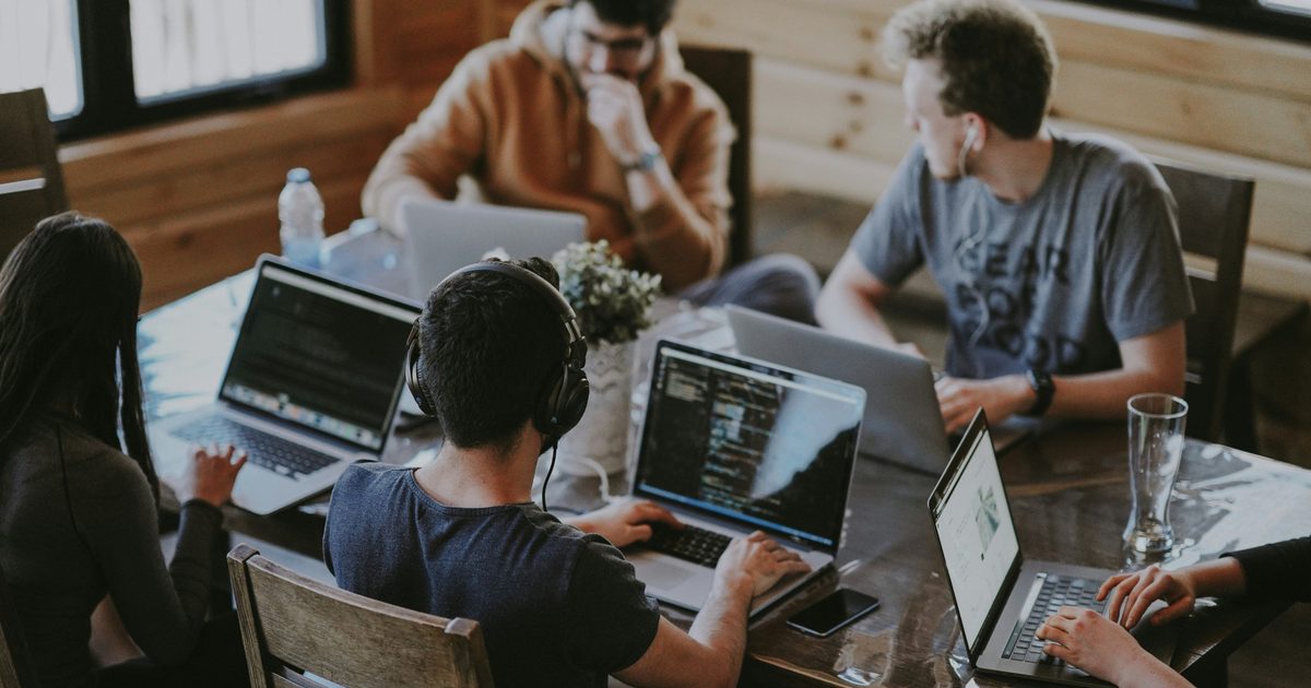 Een team werkt samen aan een houten tafel, elk op een laptop
