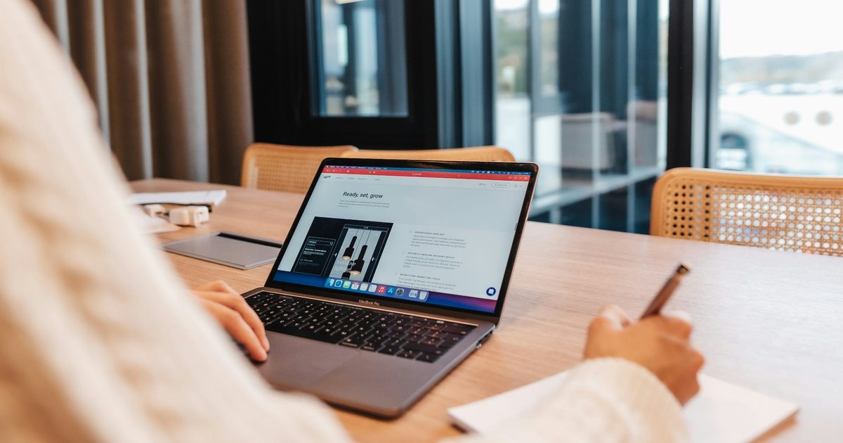 Iemand werkt aan een website op een laptop aan een houten tafel en maakt notities