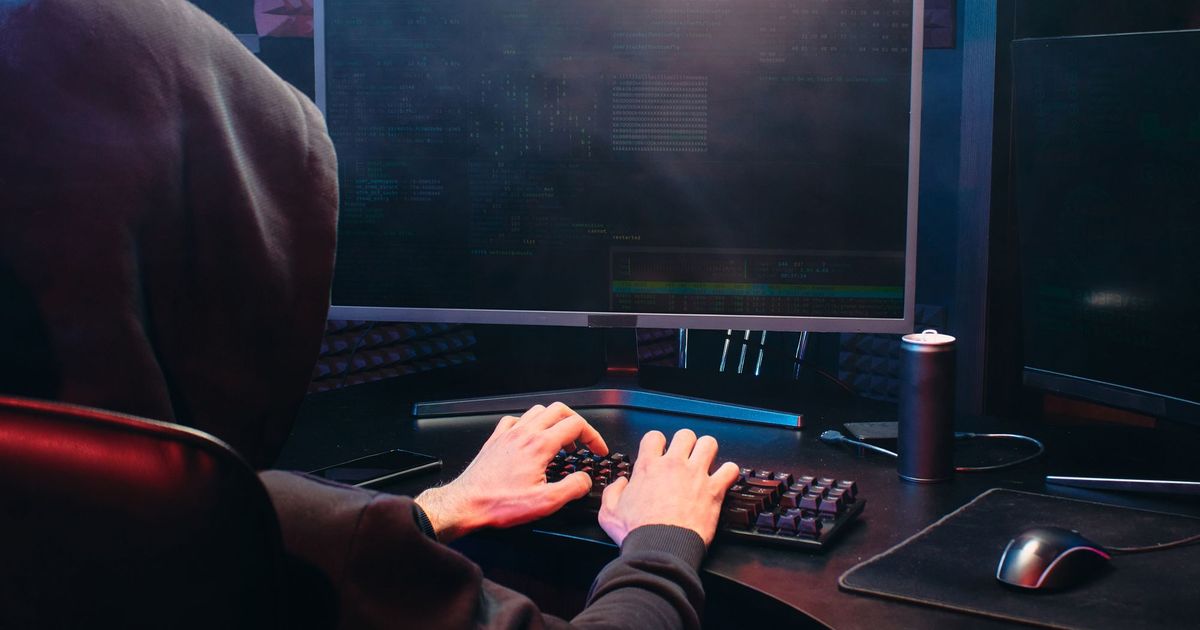 Persoon in een zwarte hoodie die typt aan een computer in een donkere kamer