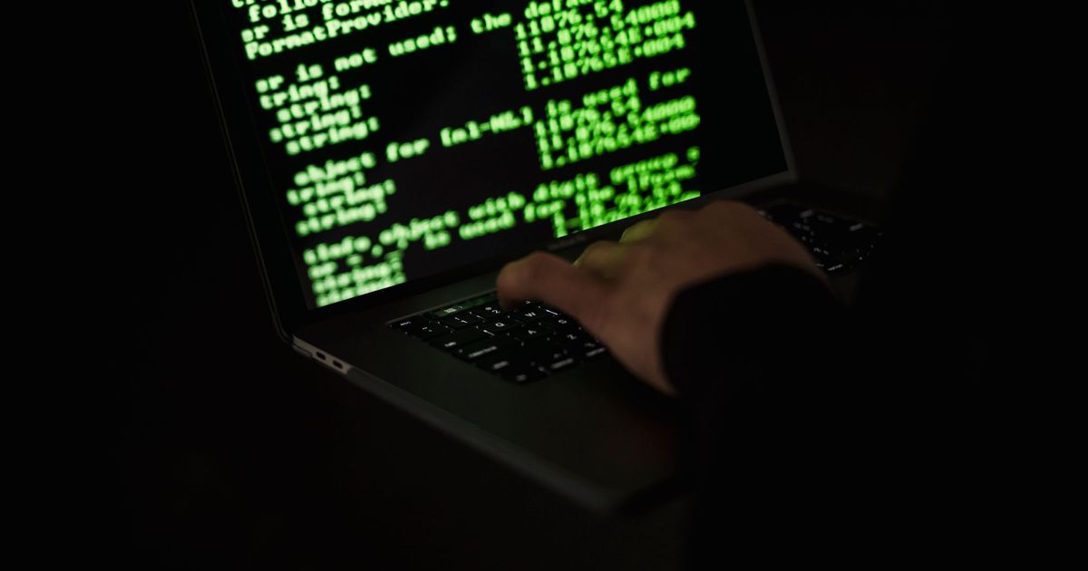 Handen op een laptop in het donker met groene code op het scherm