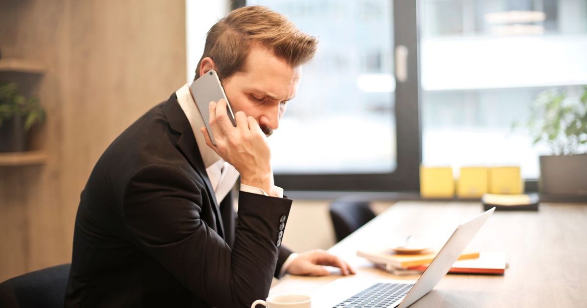 Man in pak die telefoneert aan zijn bureau met een laptop