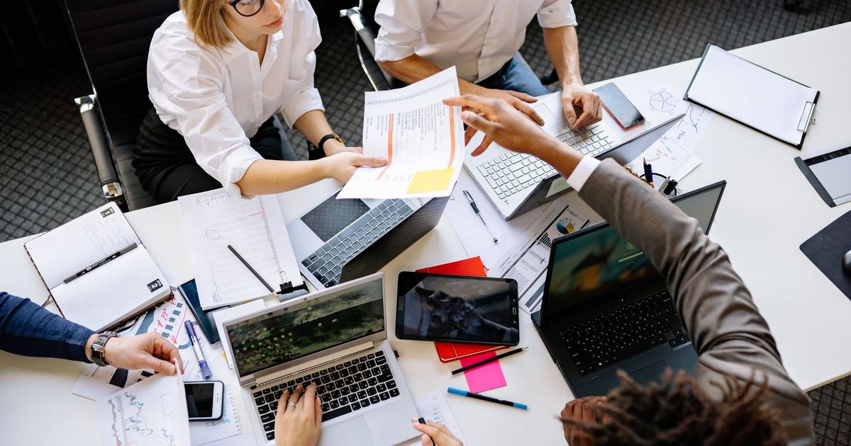 Een team werkt samen aan een tafel vol documenten en laptops