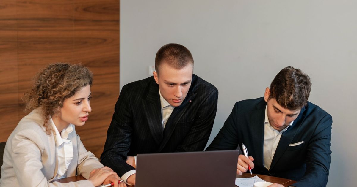 Drie collega's kijken samen naar een laptop, één van hen maakt notities