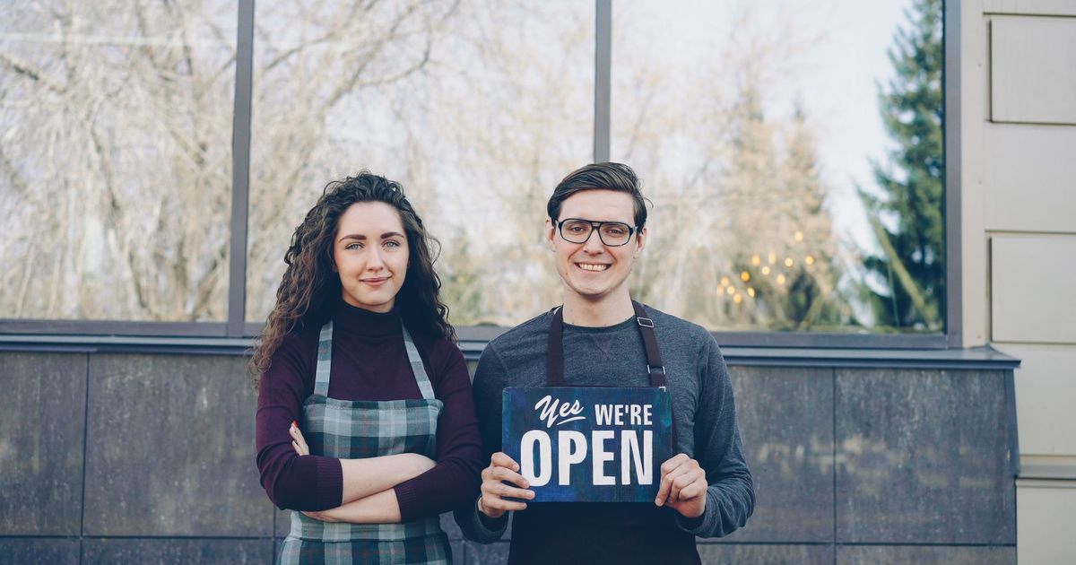 Twee zaakvoerders voor hun winkel met een bordje 'open'