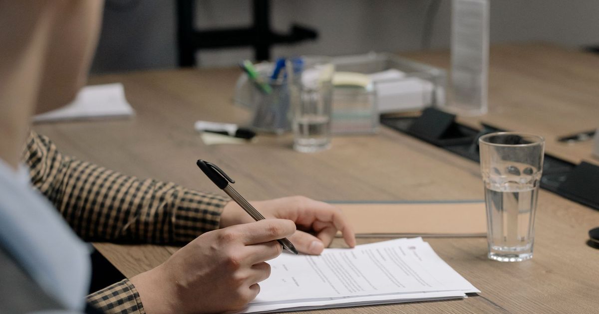 Iemand met een pen in de hand leest een contract aan een vergadertafel