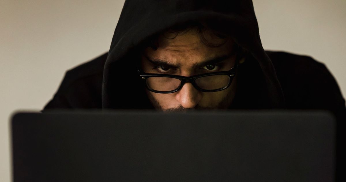 Iemand met een kap over het hoofd achter een laptop